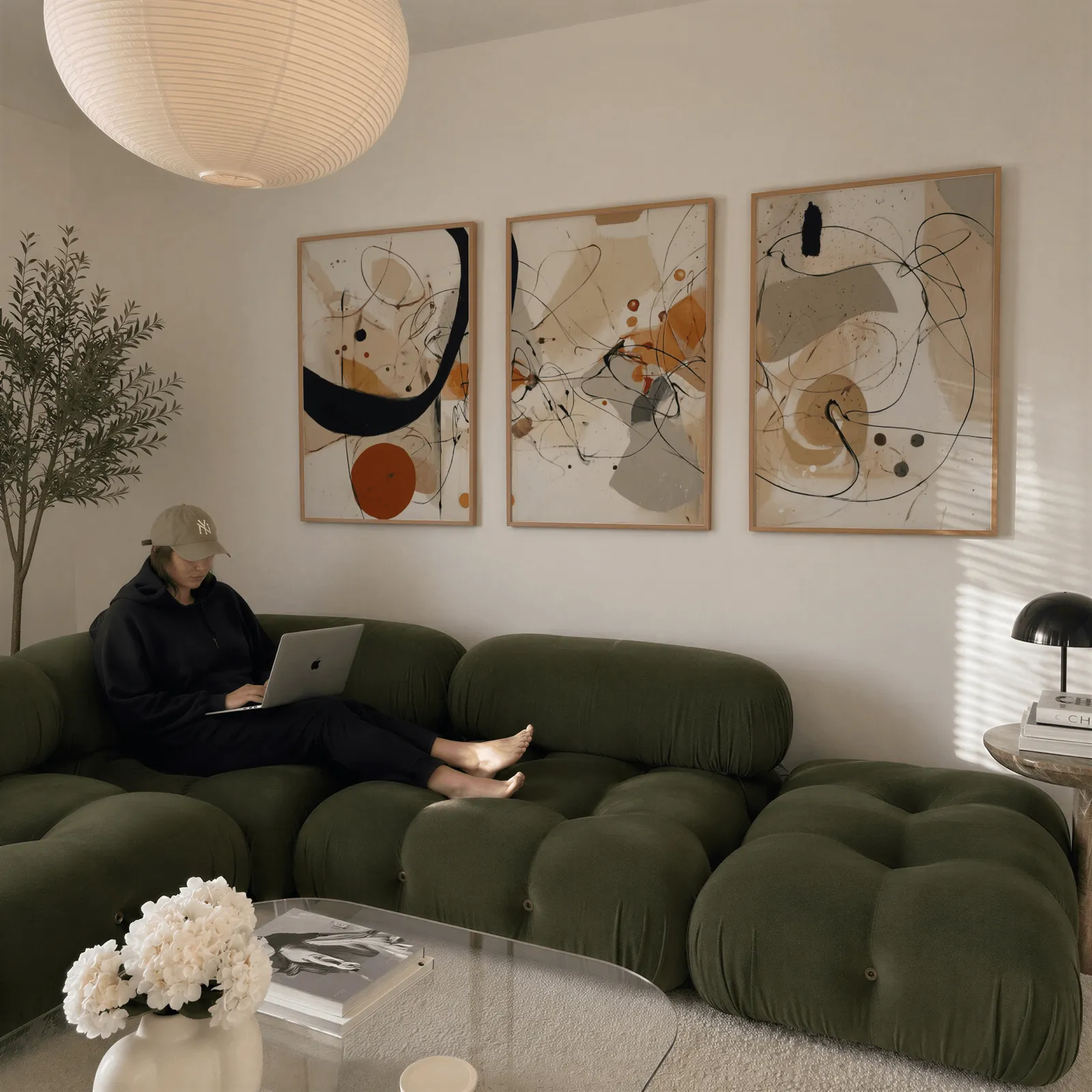 abstract terracotta and black three piece wall art, above a plush olive velvet sectional beneath a paper lantern light
