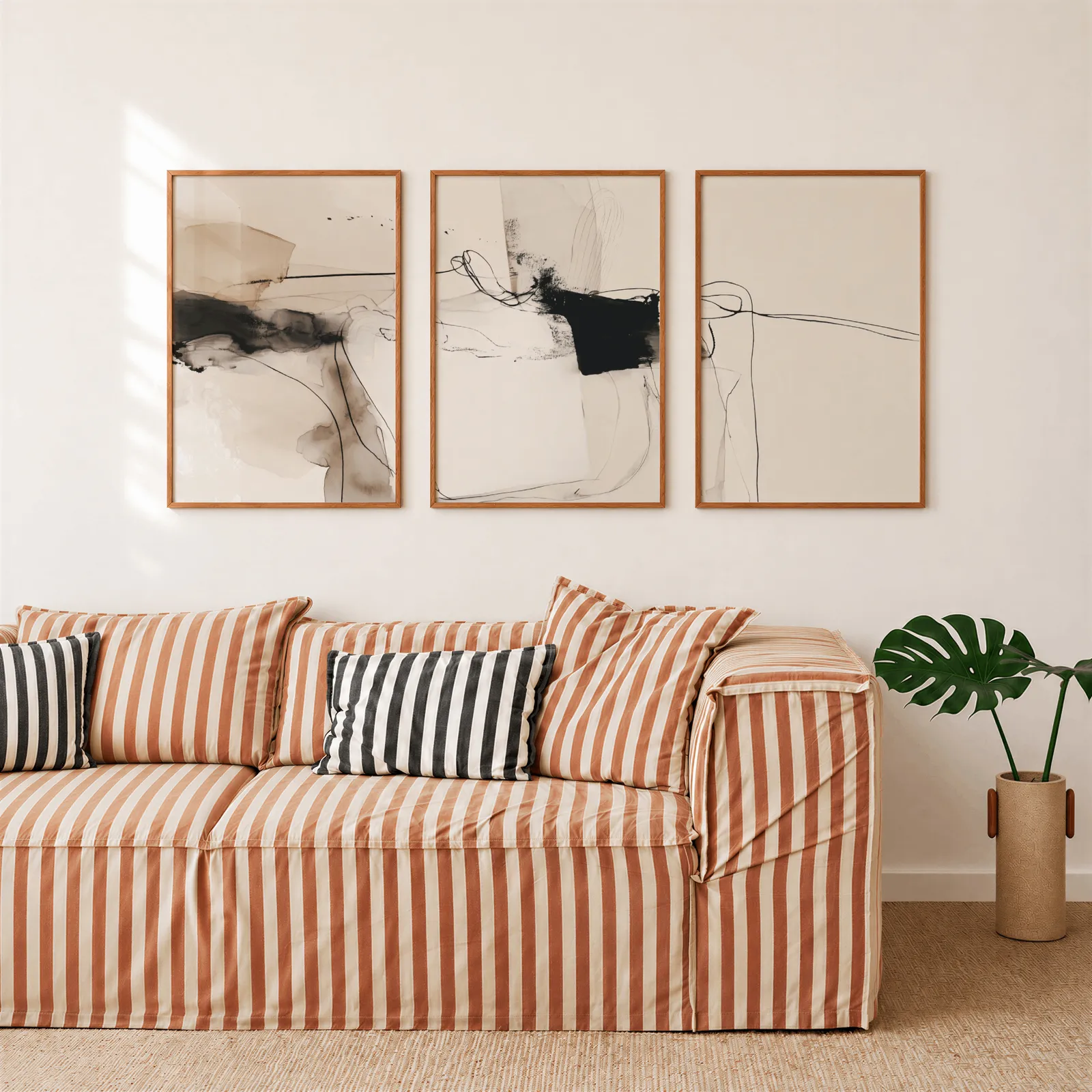 neutral abstract minimalist wall art set of 3, above a rust-striped sofa beside a potted monstera
