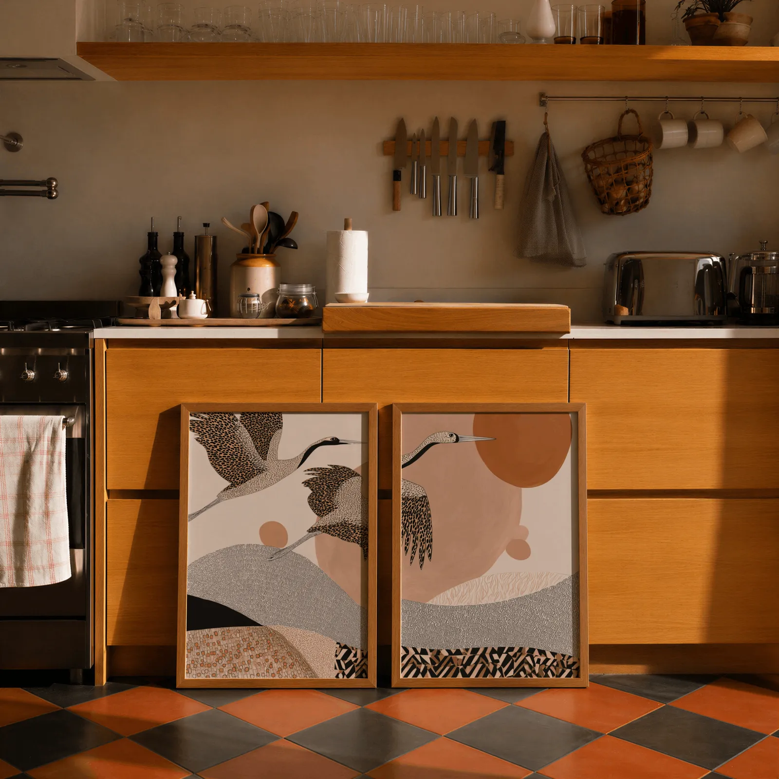 terracotta crane wall art set of two abstract landscape prints, leaning against wooden cabinets on terracotta tiled floor