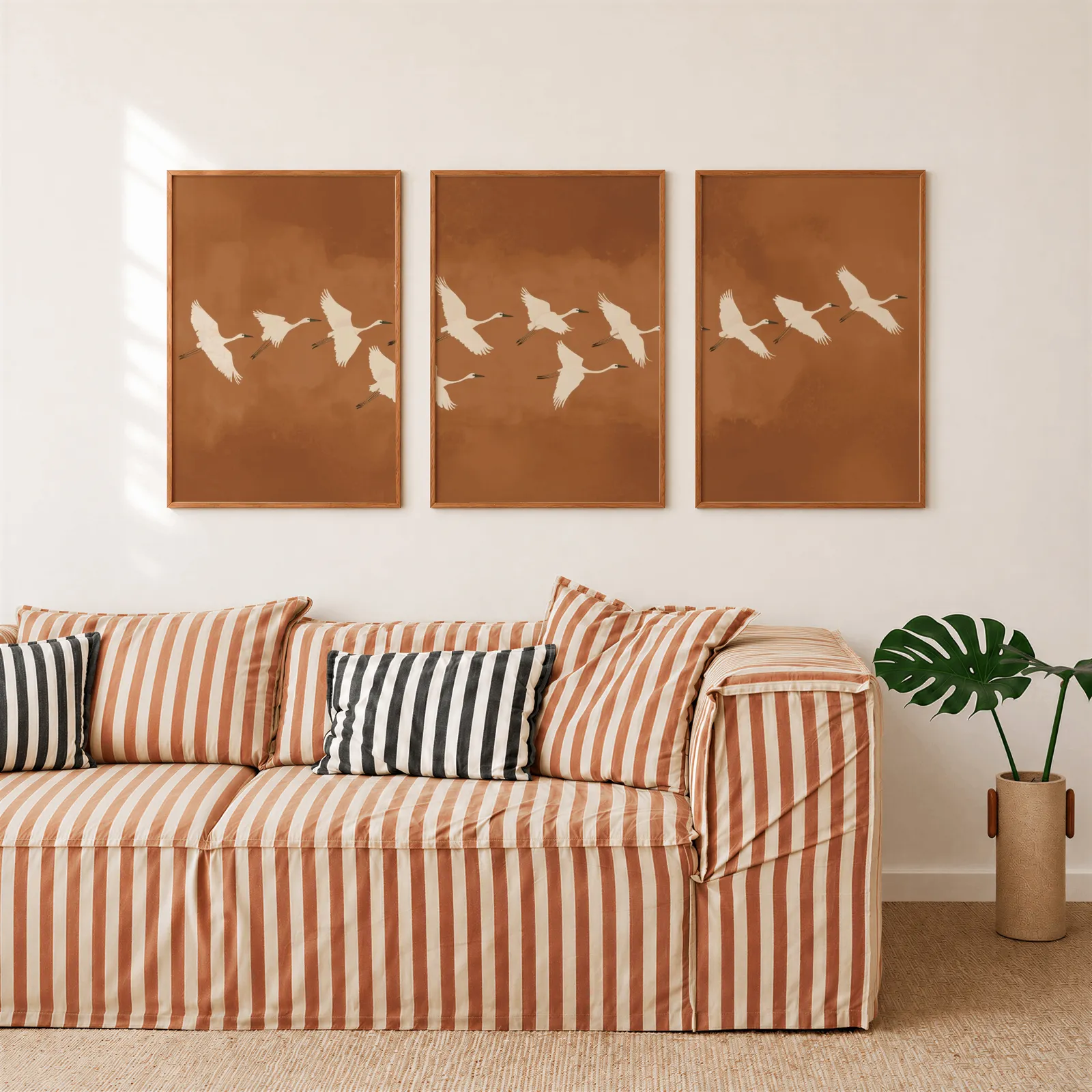 terracotta crane triptych wall art, above a rust-striped sofa beside a potted monstera