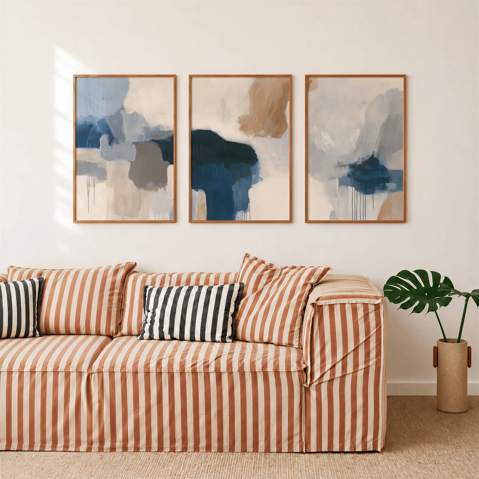 blue beige abstract triptych wall art, above a rust-striped sofa beside a potted monstera