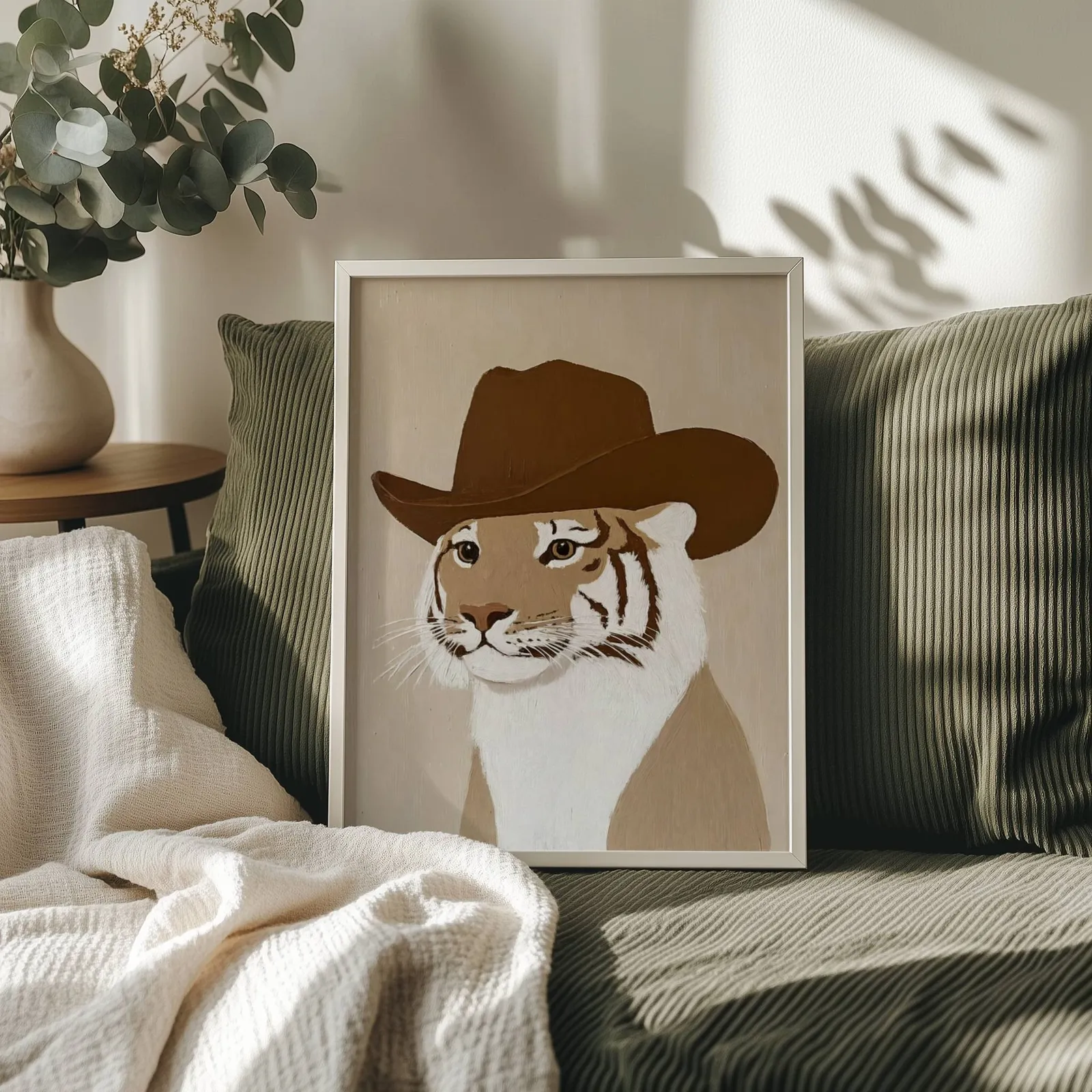 tiger in cowboy hat western wall art, propped on an olive corduroy sofa beside a eucalyptus vase