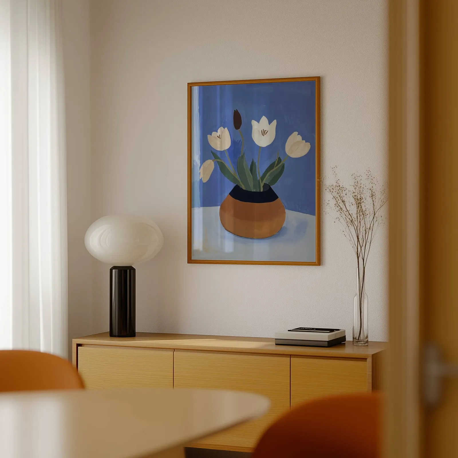 white tulips in terracotta vase botanical wall art, above a light wood sideboard beside a bulbous black lamp