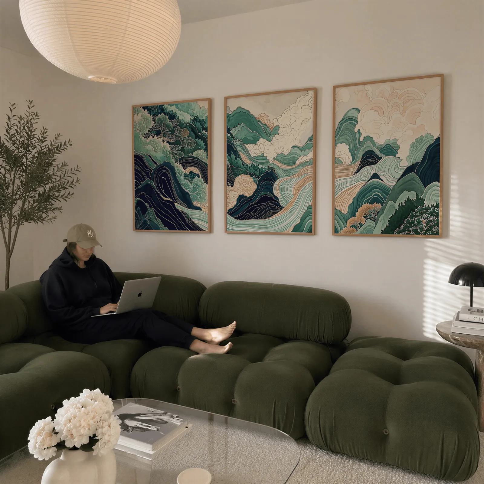 green mountain landscape wall art set of three, above a plush olive velvet sectional beneath a paper lantern light