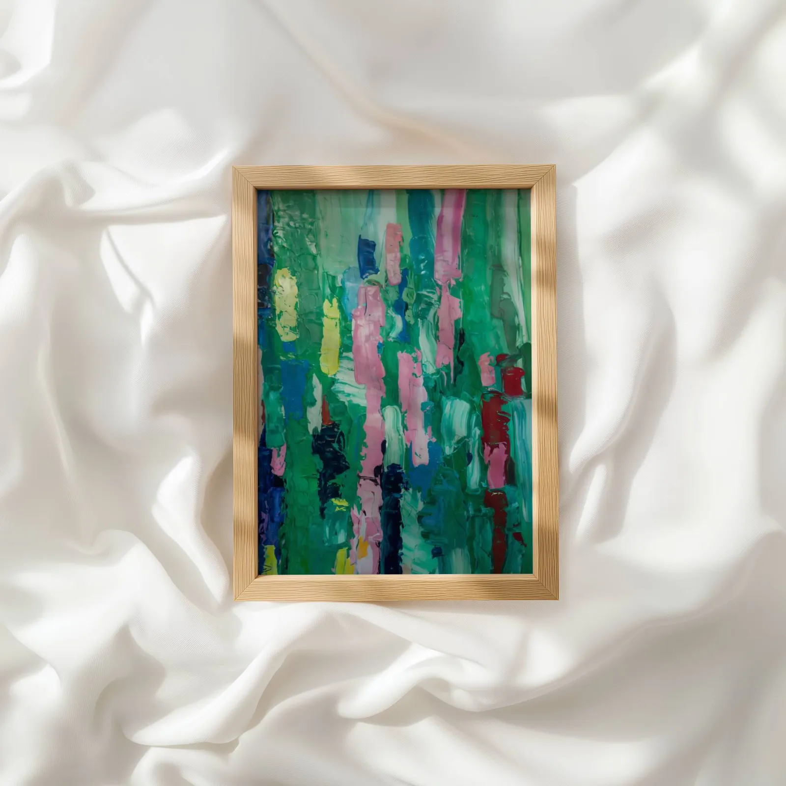colorful abstract wall art in green and pink, resting atop rumpled white silky fabric