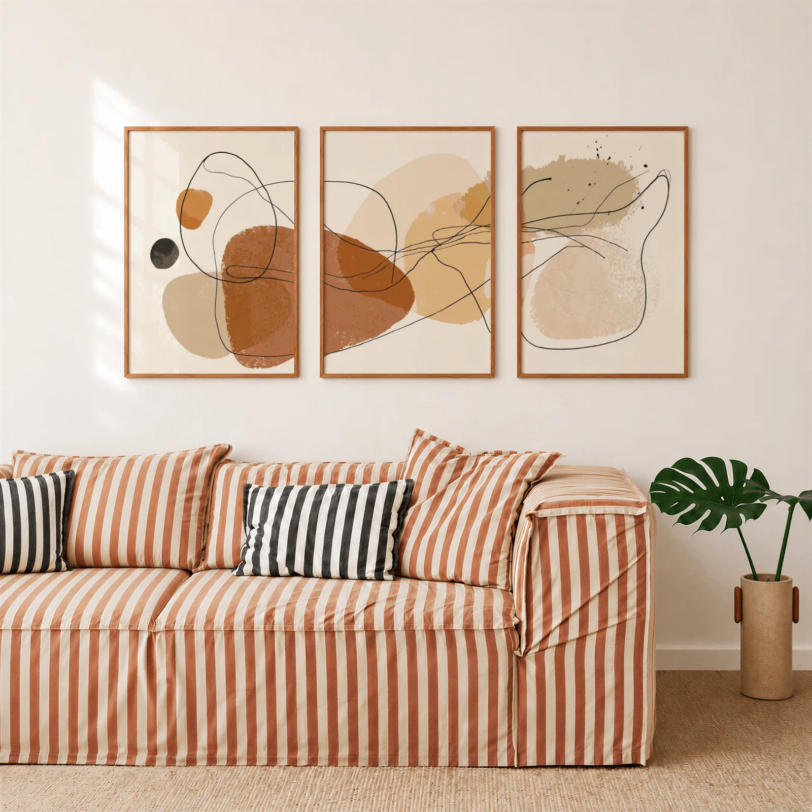 terracotta abstract minimalist wall art set of three, above a rust-striped sofa beside a potted monstera