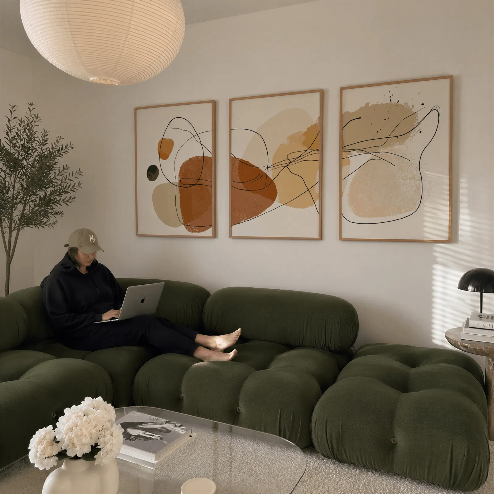 terracotta abstract minimalist wall art set of three, above a plush olive velvet sectional beneath a paper lantern light