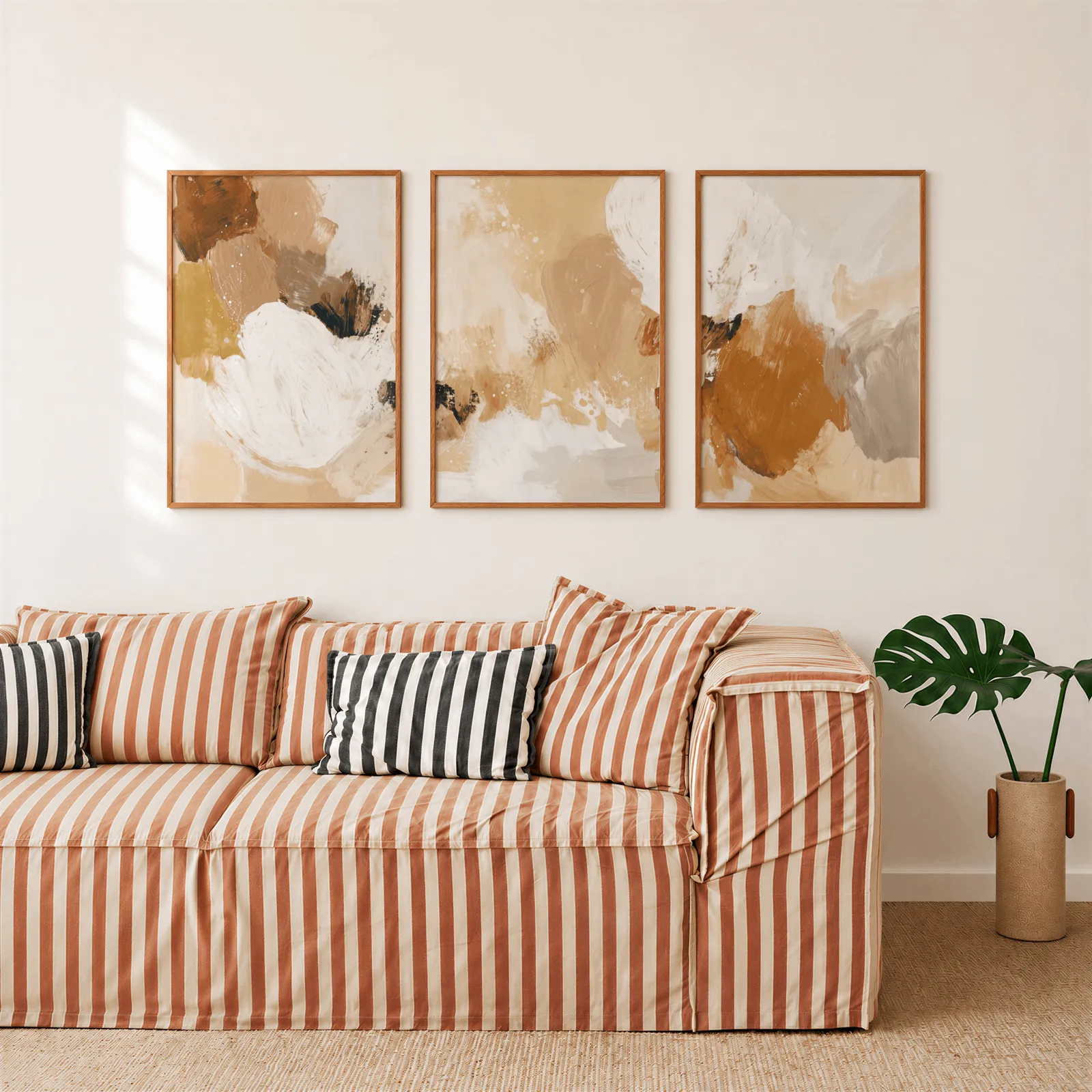 terracotta abstract three piece wall art, above a rust-striped sofa beside a potted monstera