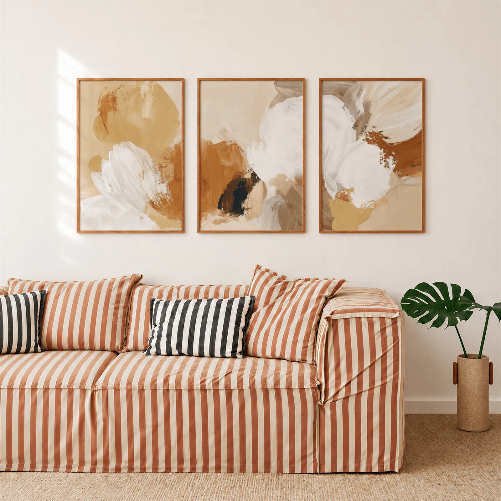 beige abstract triptych wall art set of 3, above a rust-striped sofa beside a potted monstera