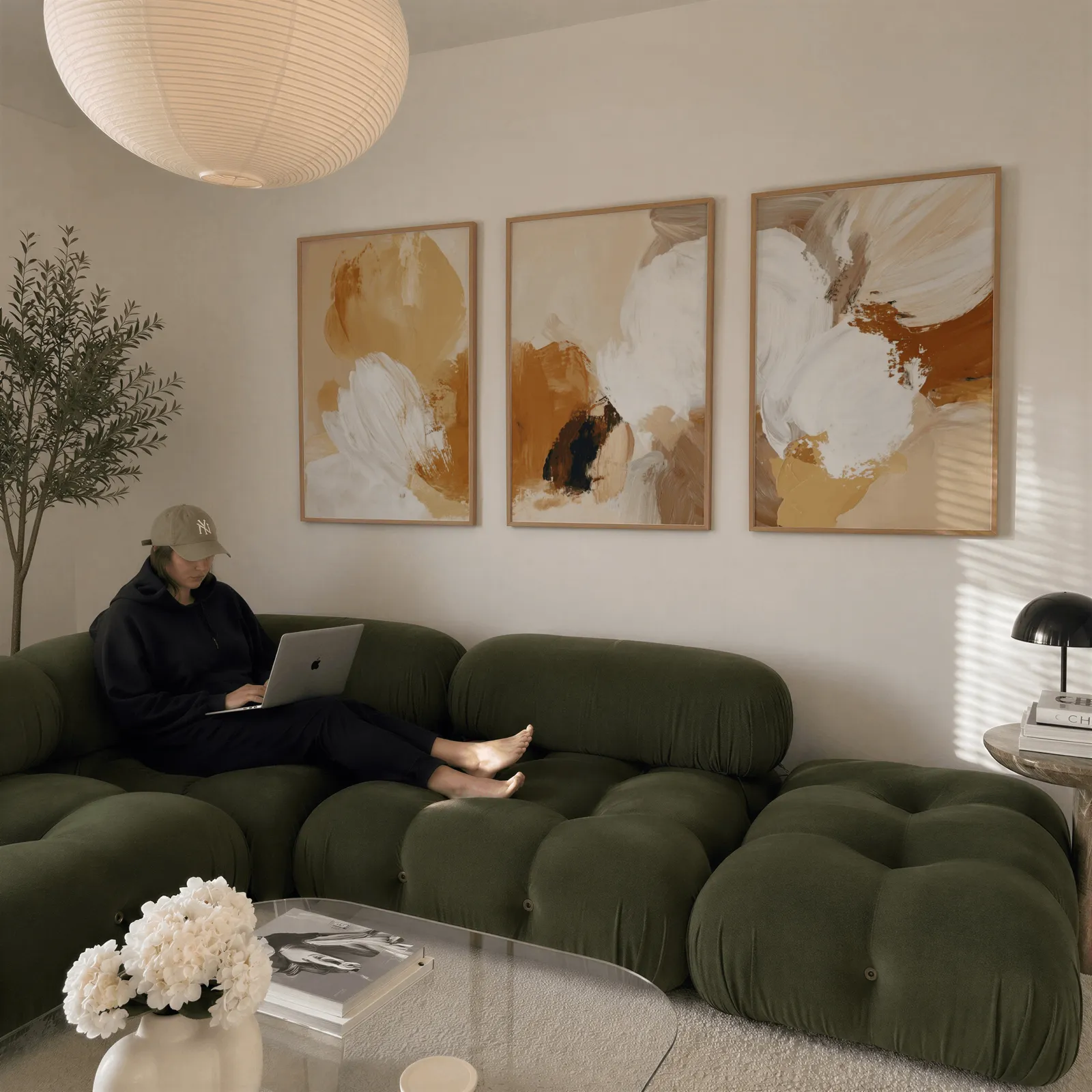 beige abstract triptych wall art set of 3, above a plush olive velvet sectional beneath a paper lantern light
