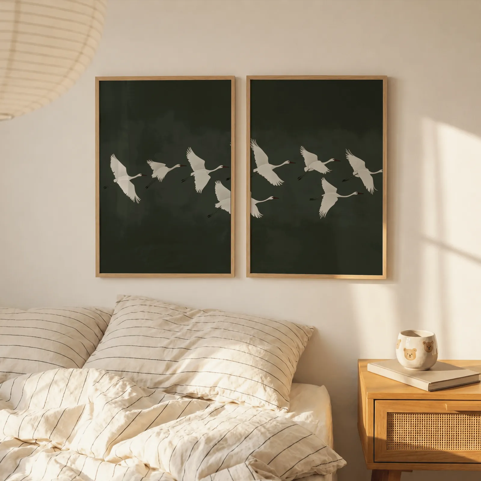 green crane wall art set of two, above a striped linen bed beside a paper lantern shade