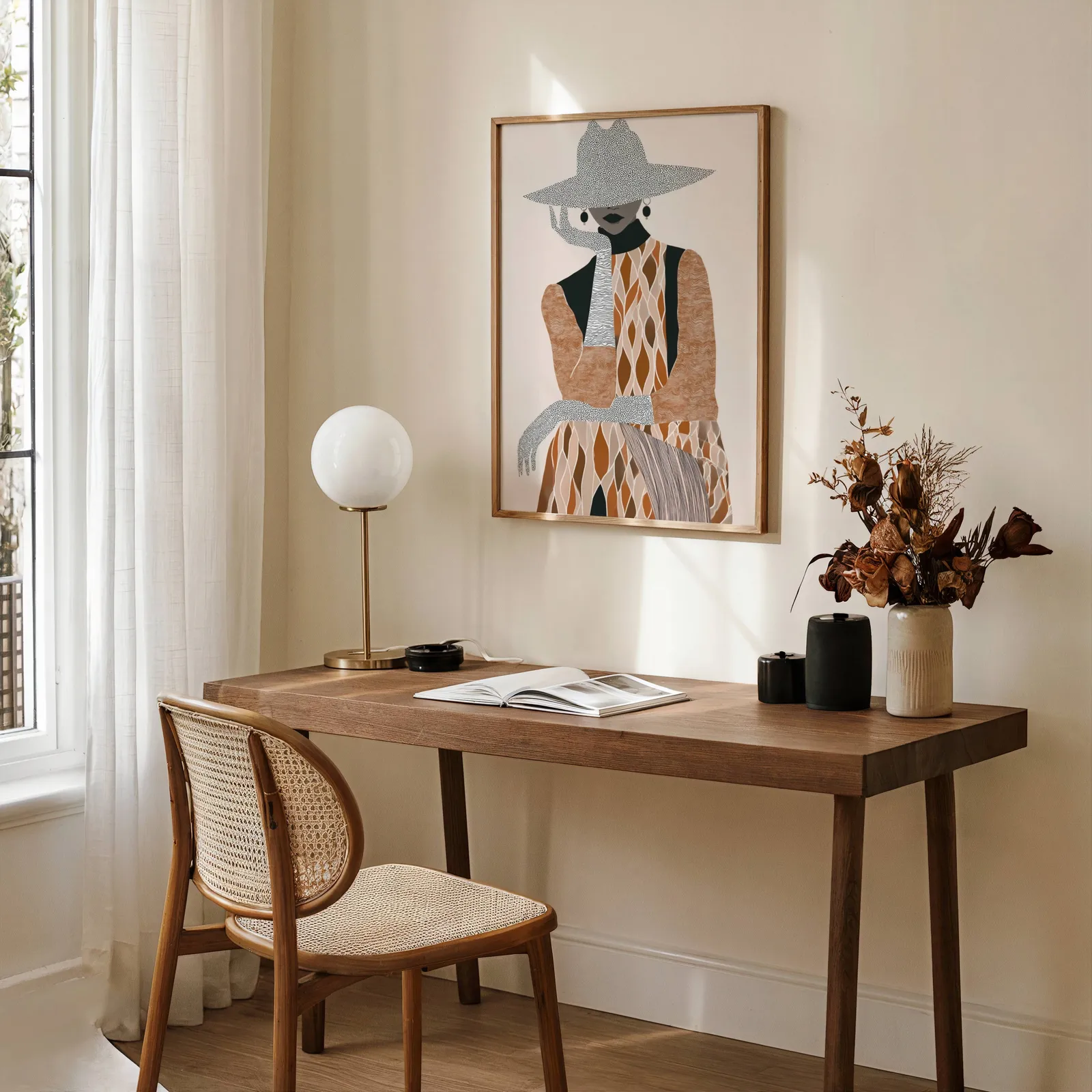 boho woman portrait wall art in brown and cream, above a wooden desk with a globe lamp and dried flowers