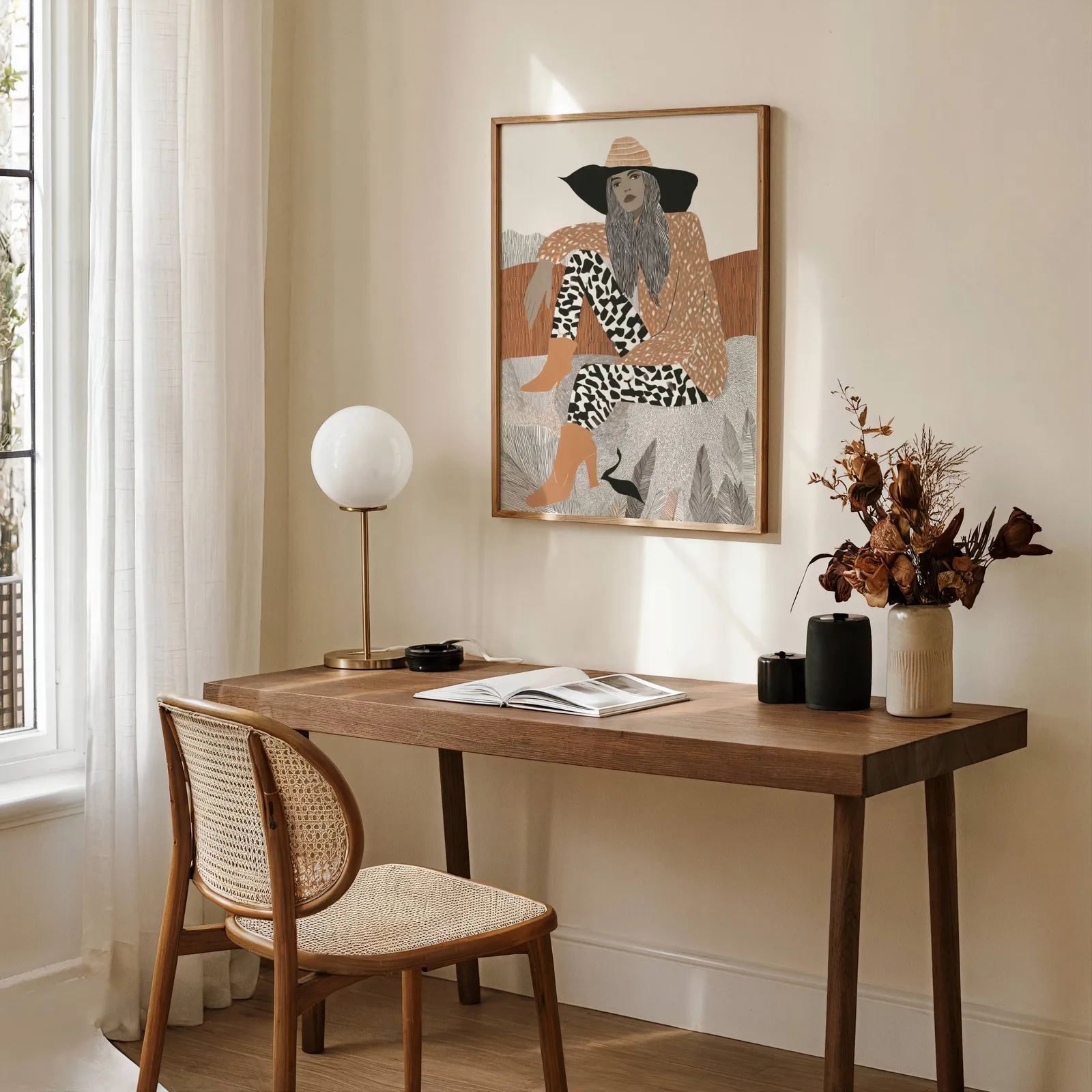 terracotta boho woman portrait wall art, above a wooden desk with a globe lamp and dried flowers