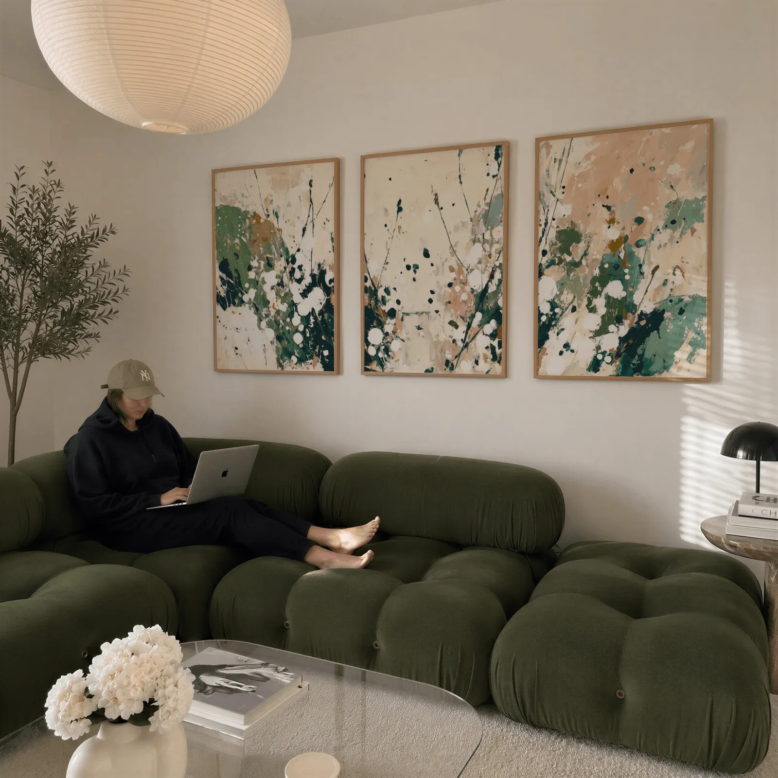 green abstract wall art set of three, above a plush olive velvet sectional beneath a paper lantern light