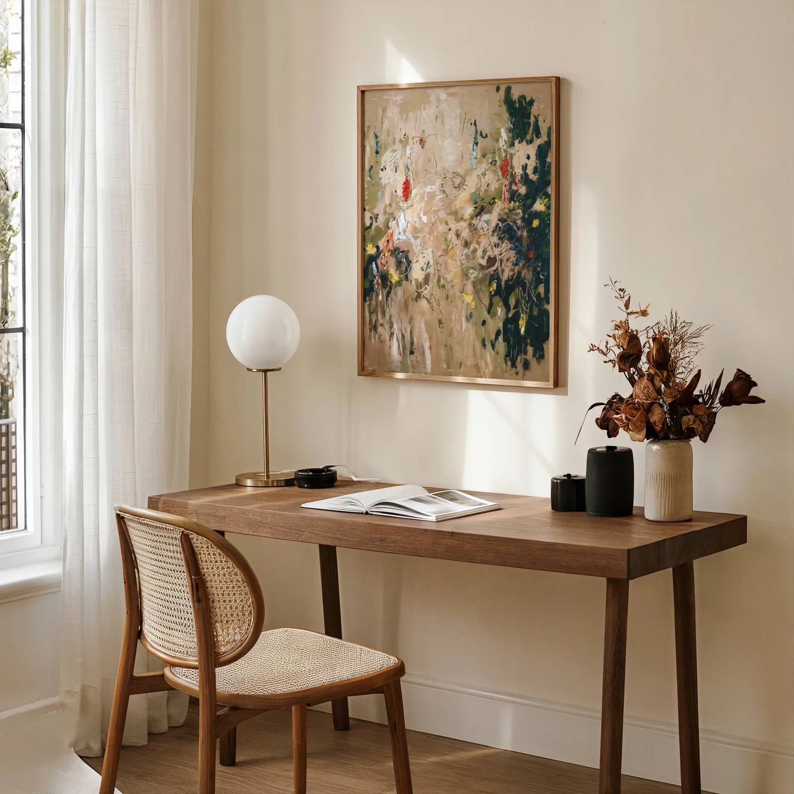 abstract floral wall art in beige and green, above a wooden desk with a globe lamp and dried flowers