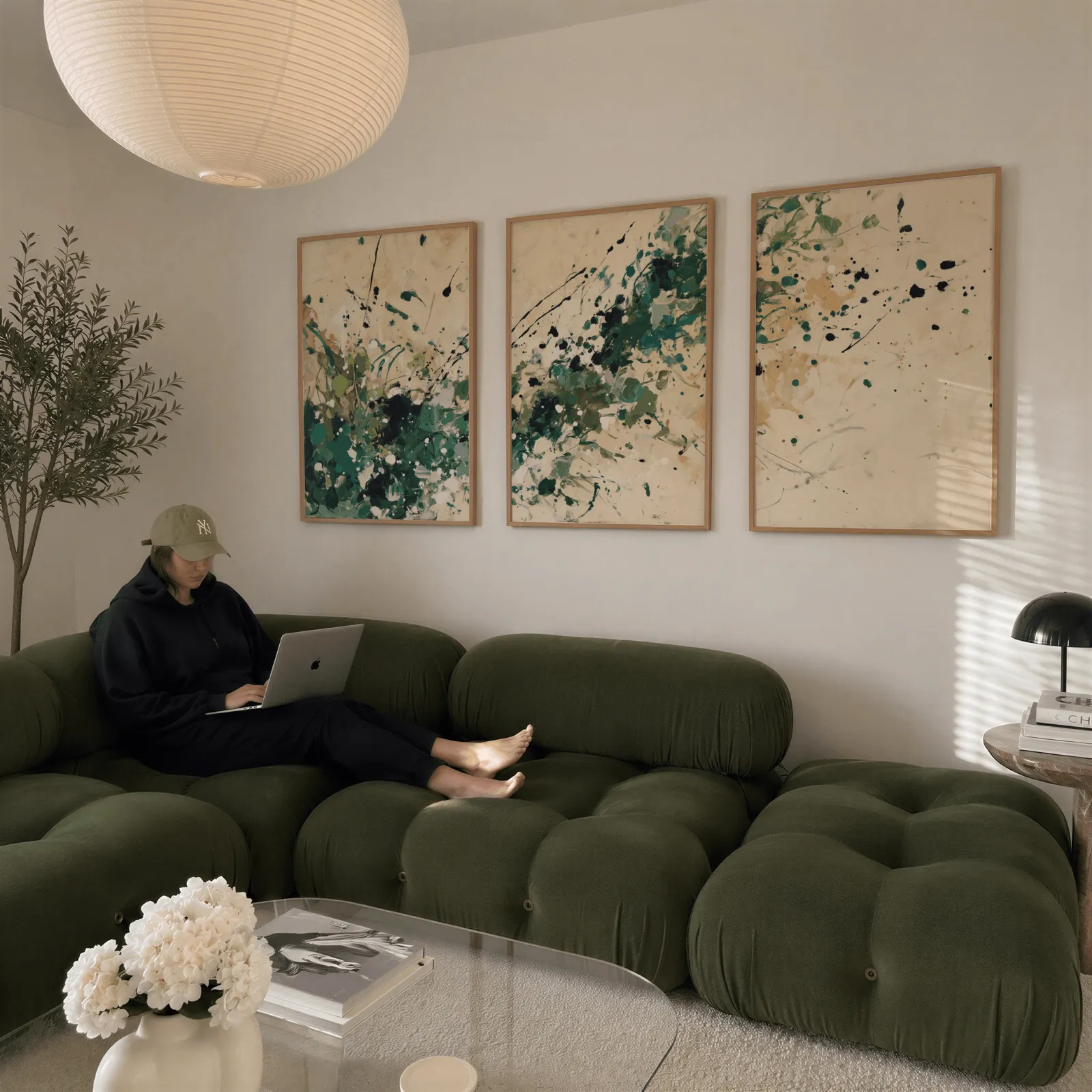 green abstract splatter triptych wall art, above a plush olive velvet sectional beneath a paper lantern light