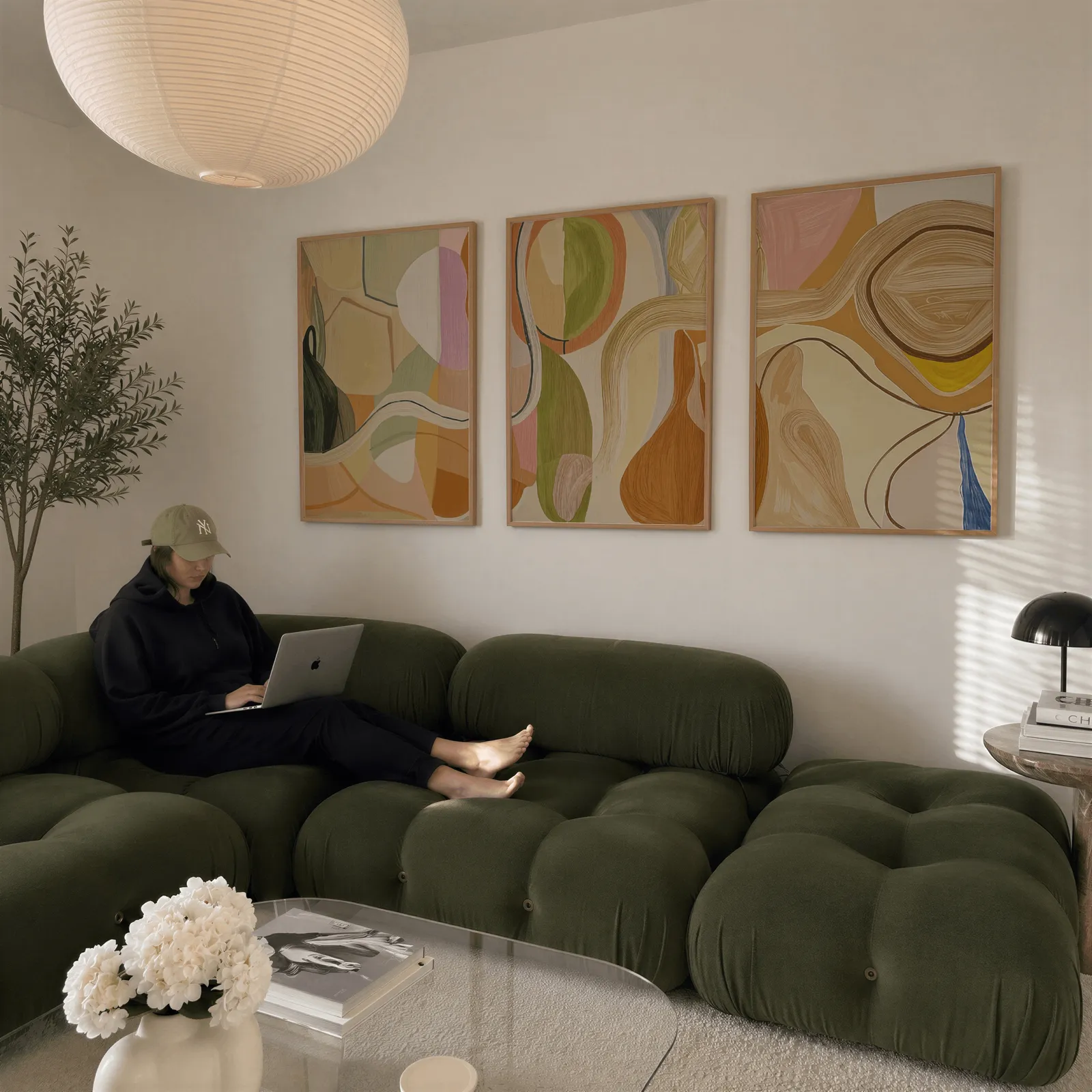 abstract terracotta and green wall art set of 3, above a plush olive velvet sectional beneath a paper lantern light