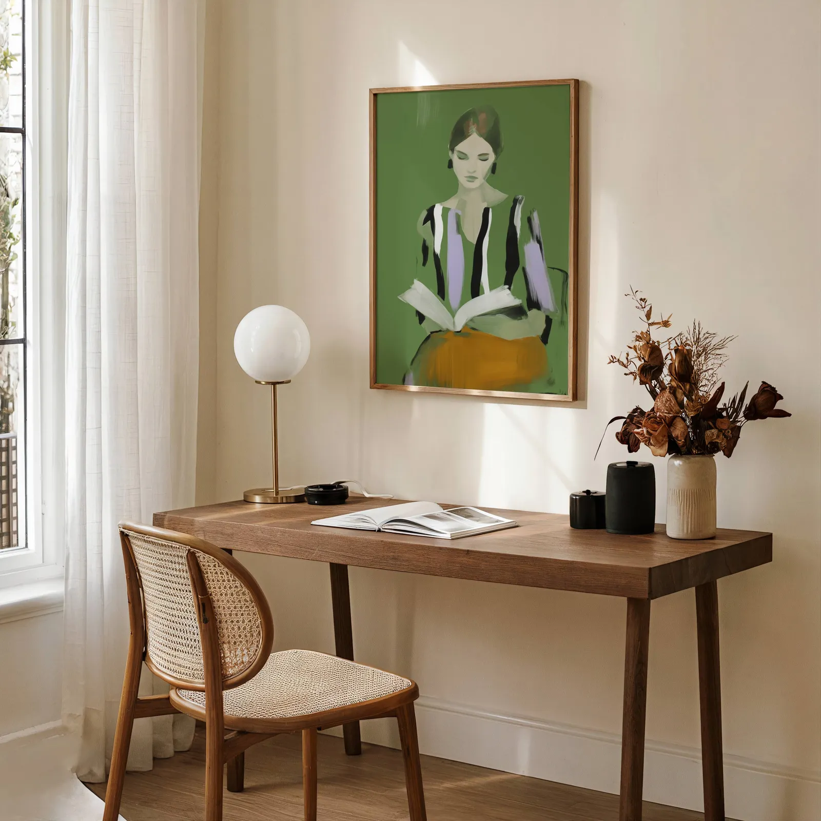 green modern woman reading wall art, above a wooden desk with a globe lamp and dried flowers