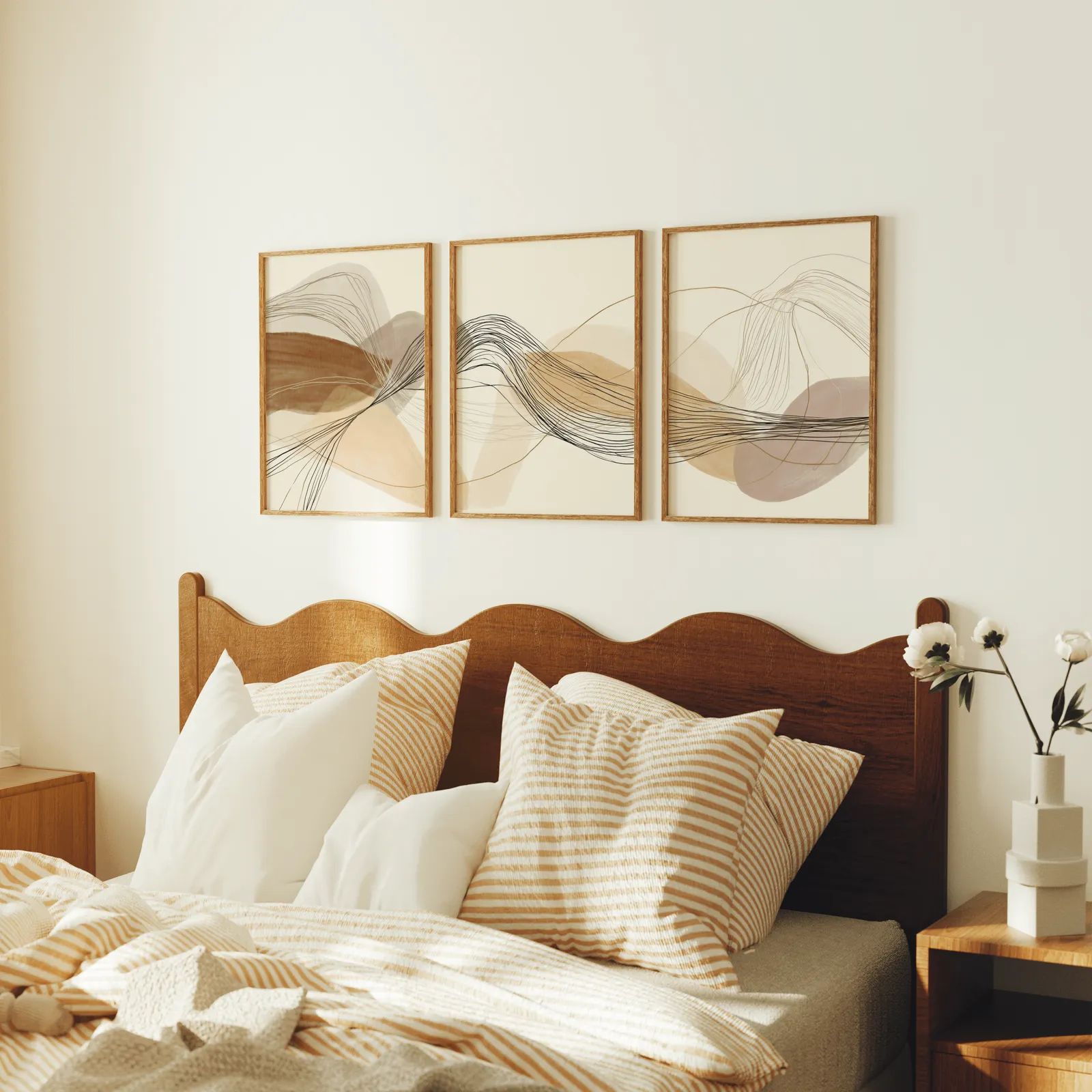 neutral abstract triptych wall art in terracotta and beige, above a scalloped wooden headboard with striped pillows