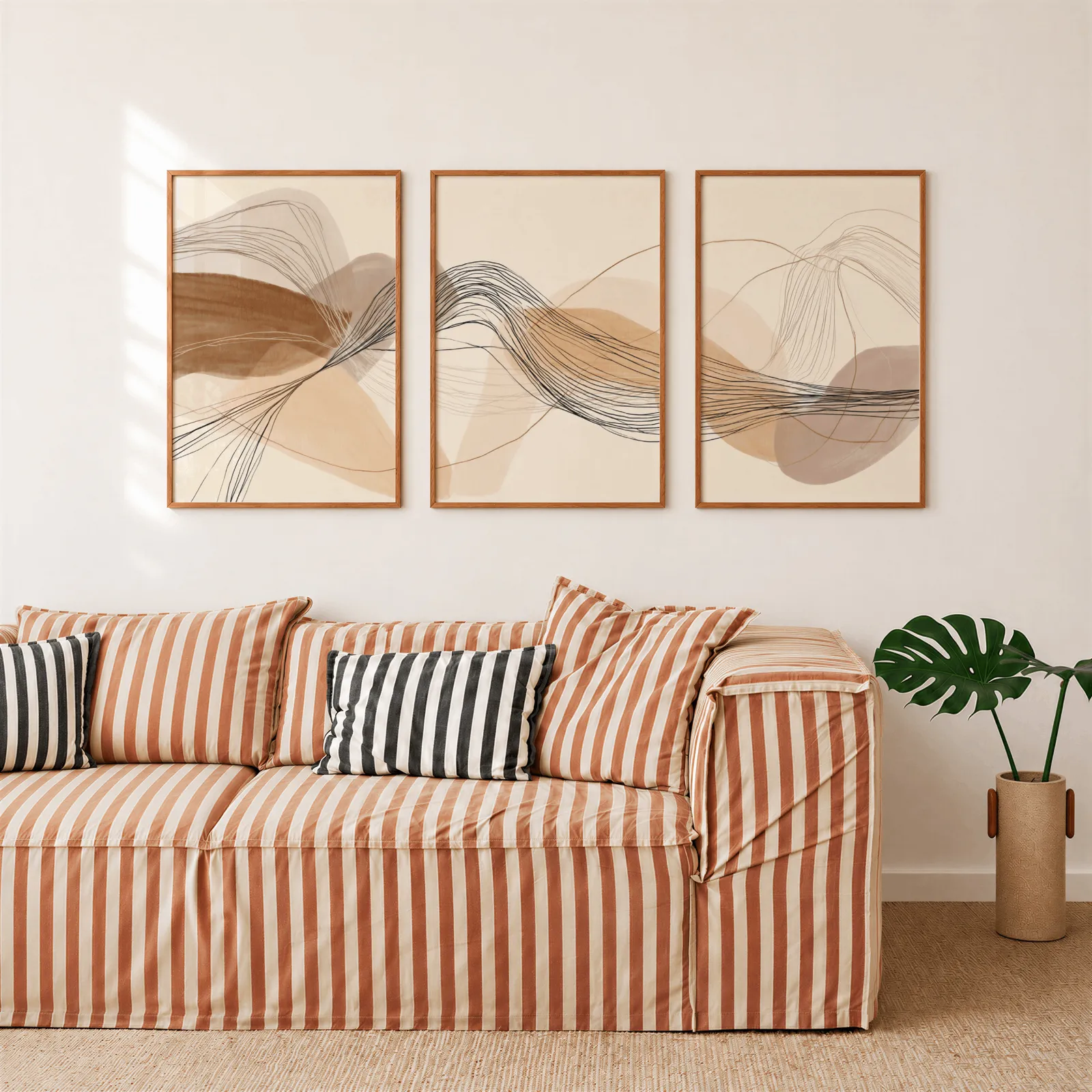 neutral abstract triptych wall art in terracotta and beige, above a rust-striped sofa beside a potted monstera