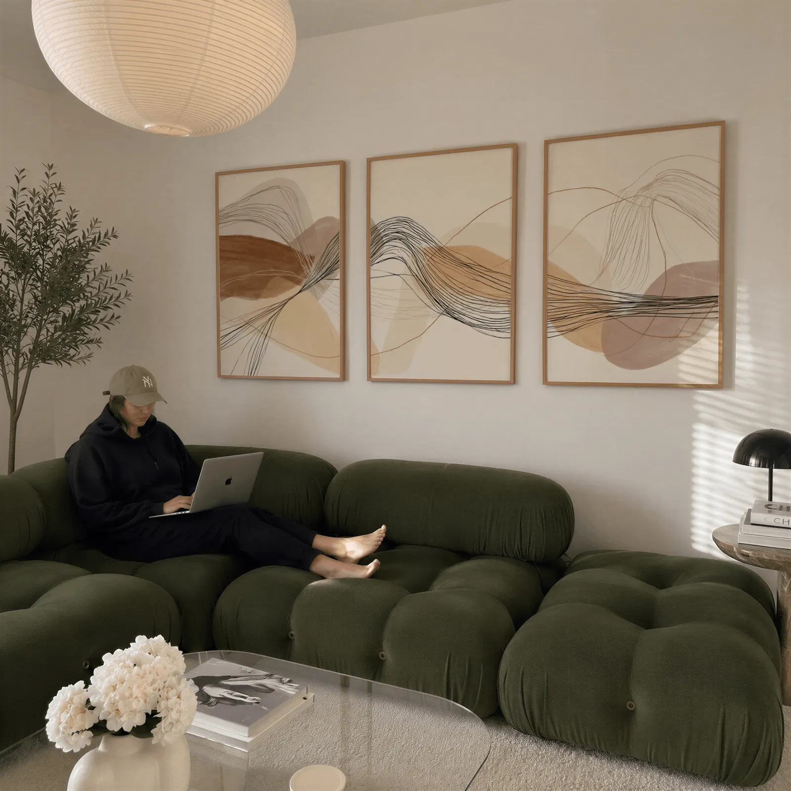 neutral abstract triptych wall art in terracotta and beige, above a plush olive velvet sectional beneath a paper lantern light