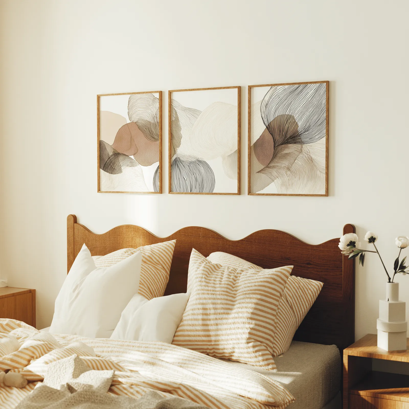 abstract three piece wall art in brown and grey, above a scalloped wooden headboard with striped pillows