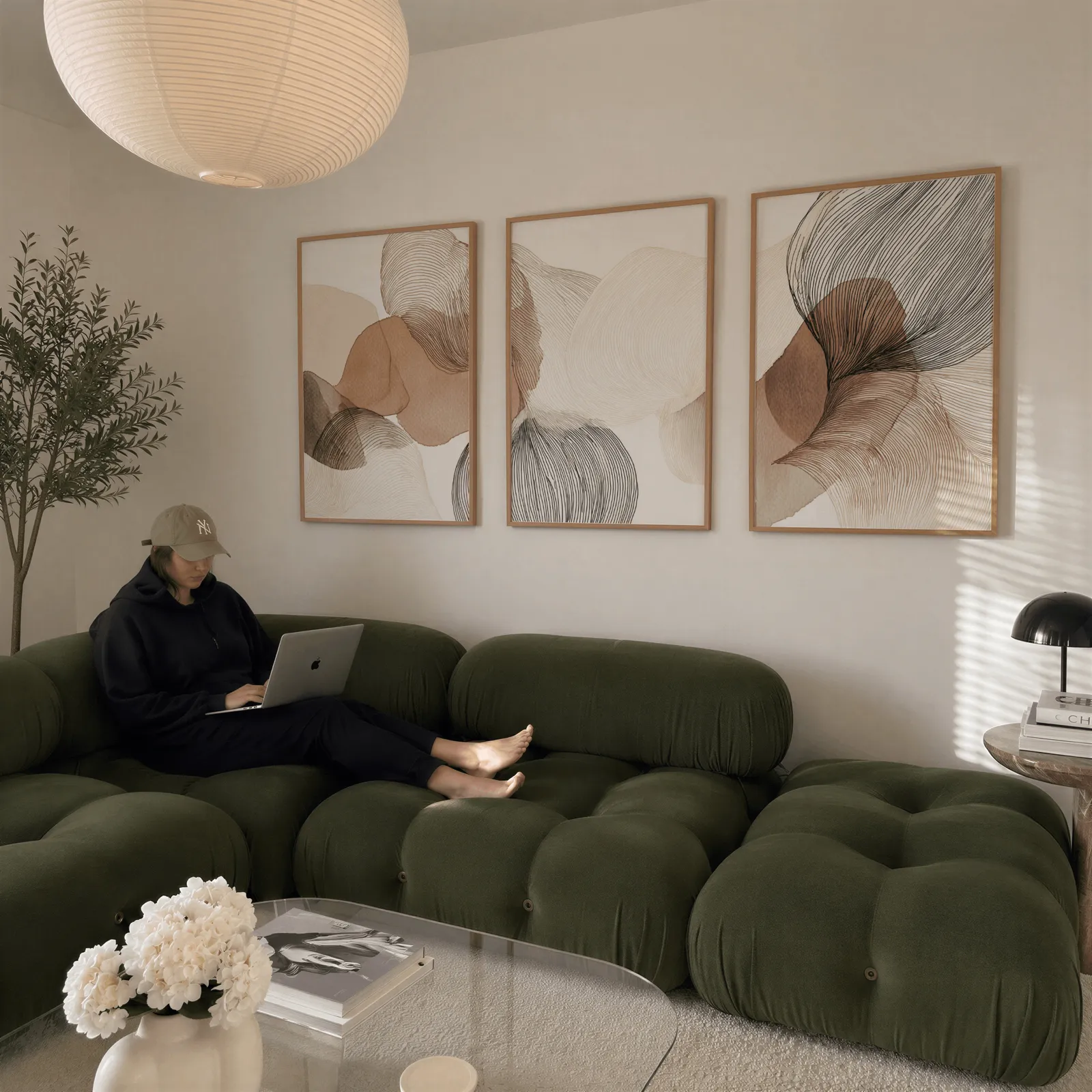 abstract three piece wall art in brown and grey, above a plush olive velvet sectional beneath a paper lantern light